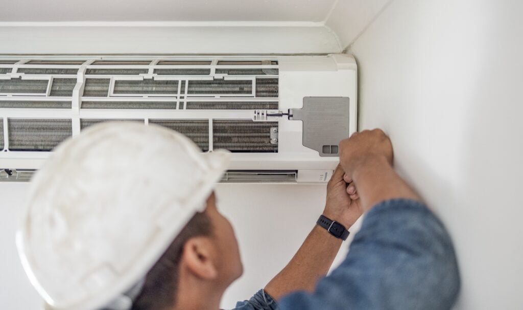 man wearing white hard hat fixing an AC unit | 7 Factors To Consider When Looking For AC Repair in San Antonio