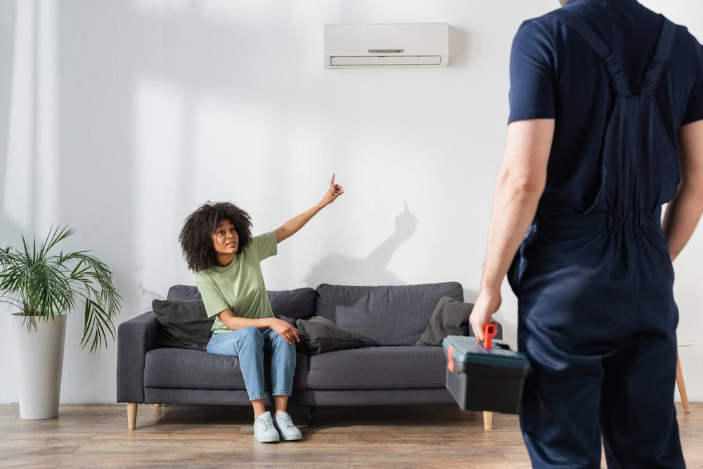 Woman pointing at broken air conditioner near handyman with toolbox - emergency conditioner repair